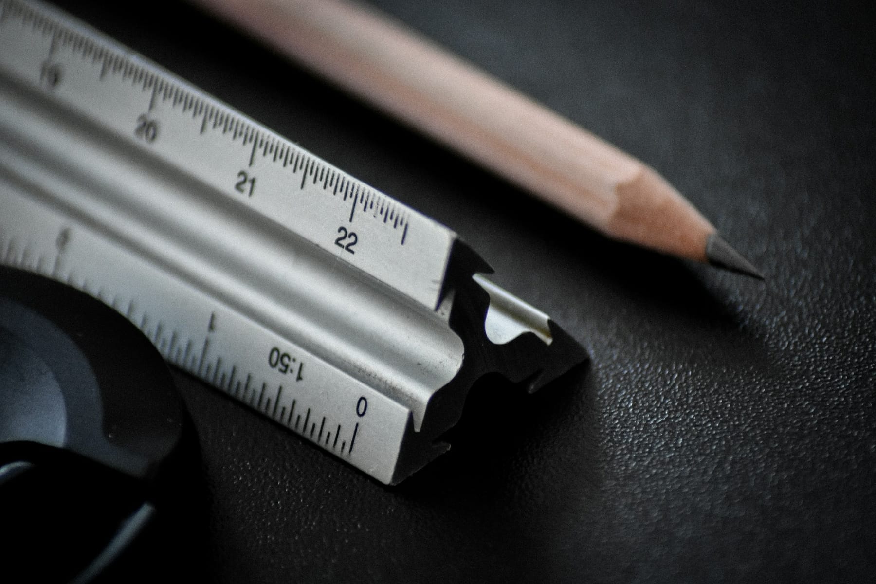 A triangular architect's scale rule and a pencil on a dark drawing surface.