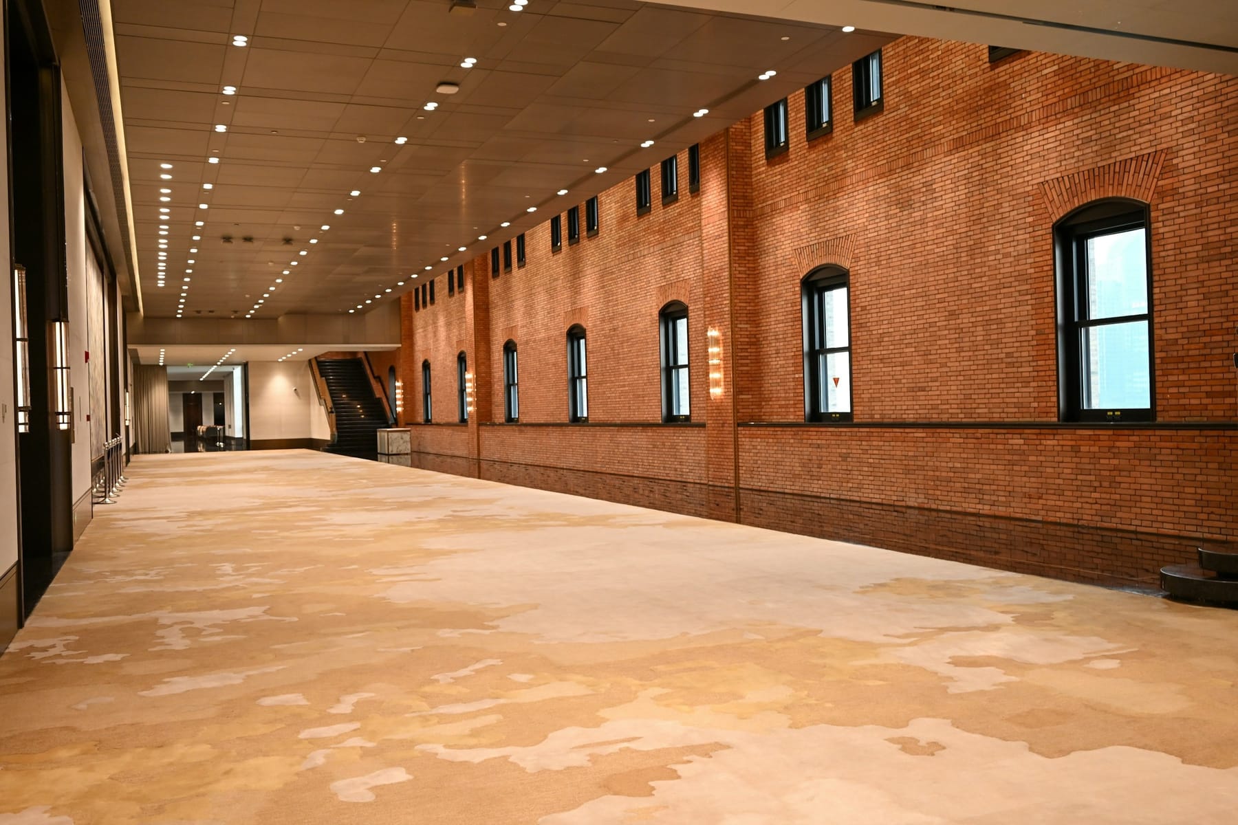 A long empty hall with exposed brick walls, a run of small windows and a bare wooden floor.