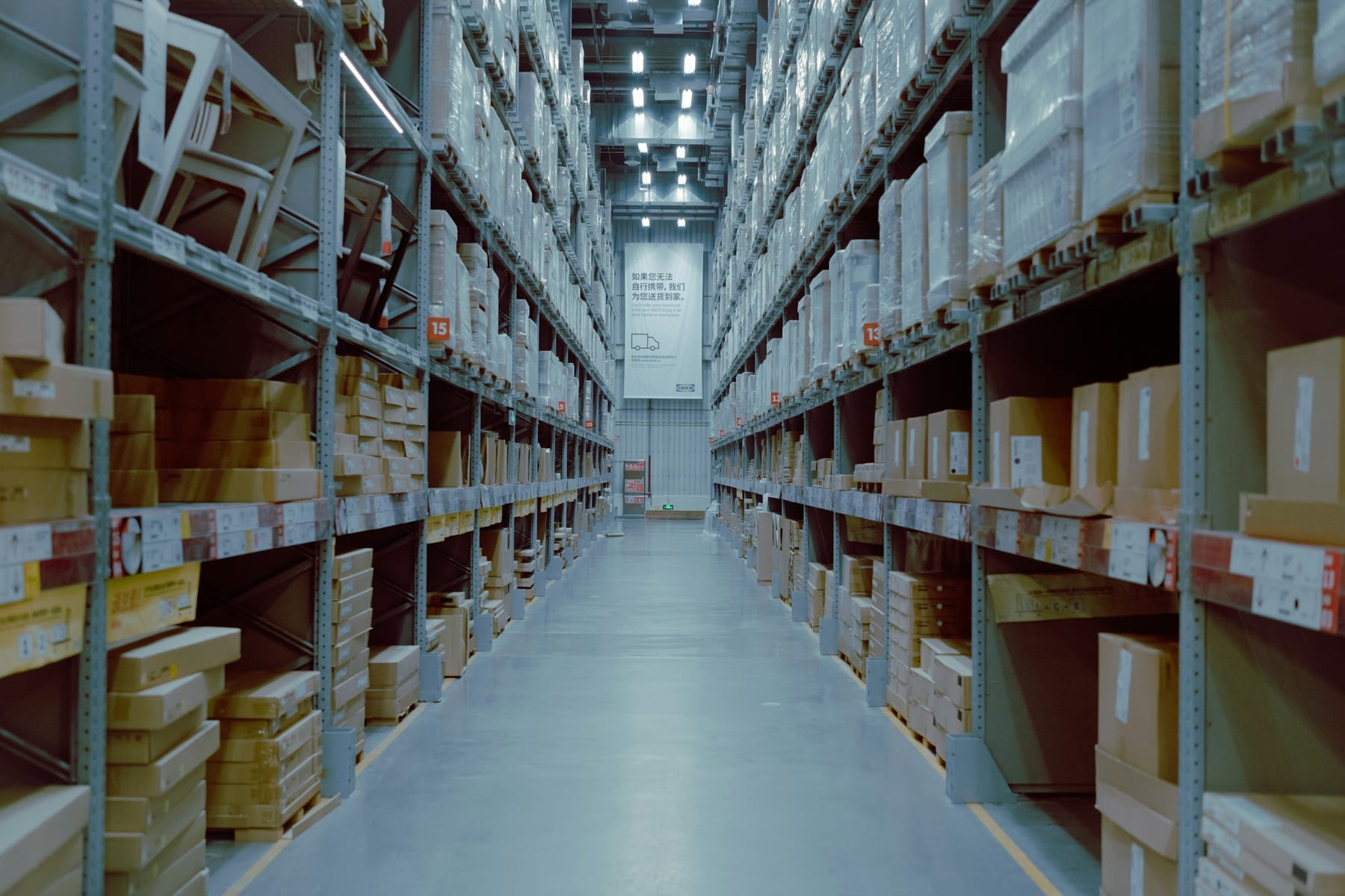 An aisle of pallet racking in a working warehouse, stacked to the roof on both sides.